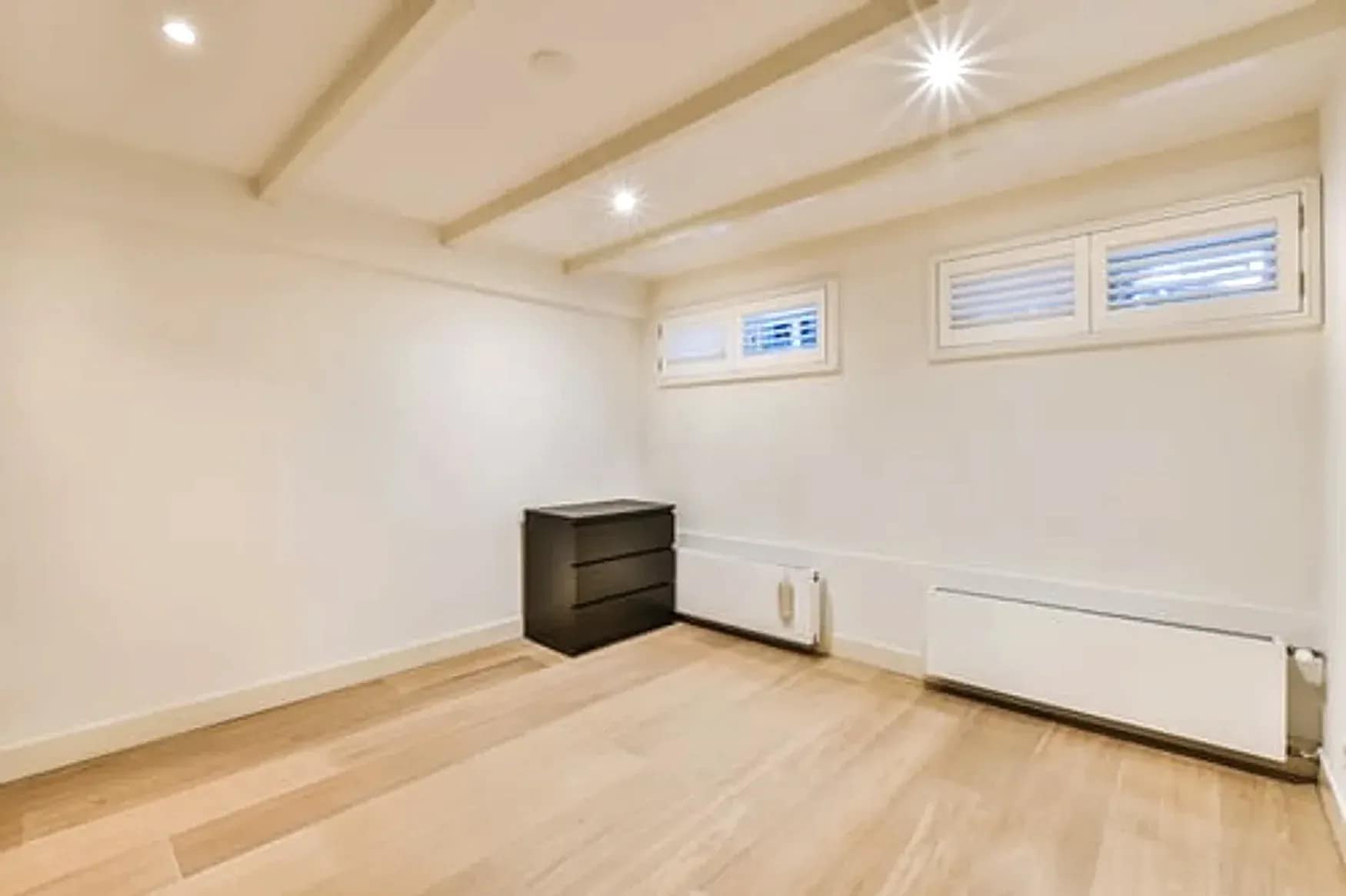 Finished basement in Maryland with light wood flooring, recessed lighting and egress windows completed by Falcon DMV Construction