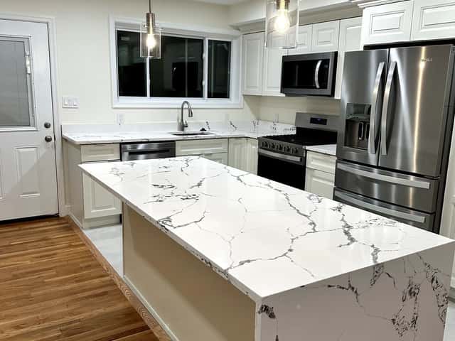Open kitchen remodel with a white quartz island, white cabinets and stainless appliances