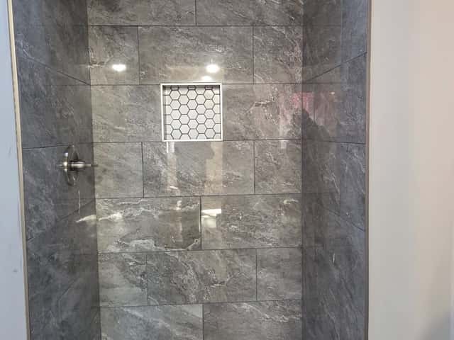 Walk-in shower tiled in grey stone with a mosaic niche