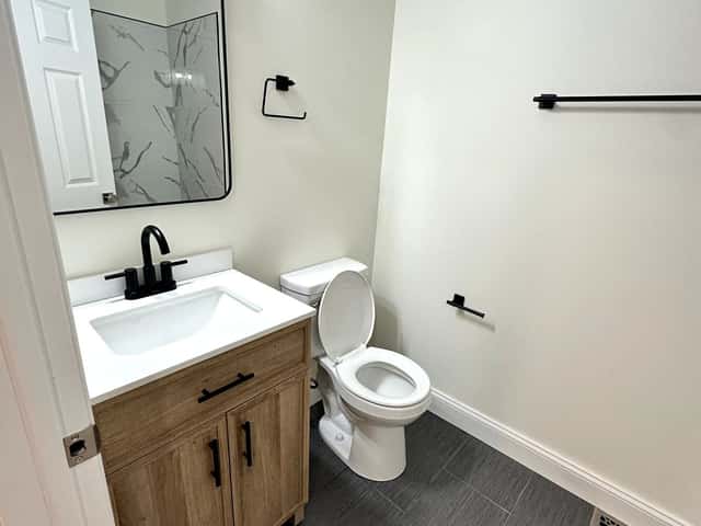 Small bathroom remodel with a wood vanity, black fixtures and a marble-look shower wall