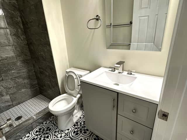 Bathroom renovation with a patterned tile floor, grey vanity and marble-look shower