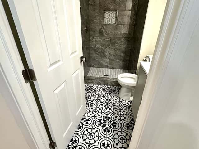 Powder room remodel with a black-and-white patterned tile floor and stone shower