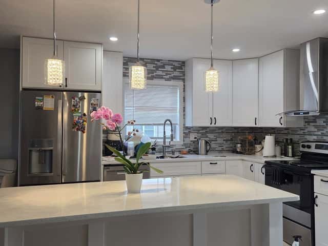 Kitchen renovation with white cabinets, a glass-tile backsplash and pendant lights over the island