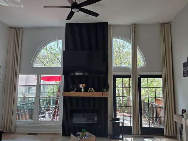 Living room renovation with a dark tile fireplace wall, ceiling fan and arched windows